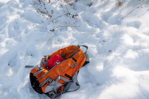 An orange backpack is laying in the soft, white snow, creating a colorful contrast against the winter landscape, inviting thoughts of adventures and fun while playing in the snow photo