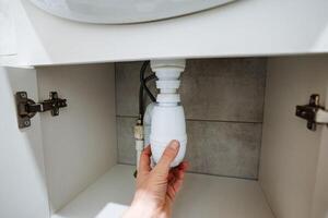 An individual is currently positioned under a bathroom sink, gripping the drain tightly in an effort to resolve what appears to be an unexpected plumbing issue that has arisen photo