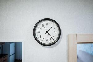 In a bright and welllit room, there is an elegantly designed clock gracefully hanging on the pristine white wall, perfectly blending and harmonizing with the decor surrounding it photo