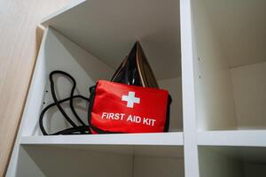 A comprehensive first aid kit is conveniently on a shelf next to an iron, ready for immediate access in case of minor injuries or emergencies, ensuring safety and peace of mind photo
