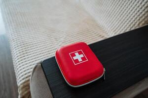 A red first aid kit, clearly marked with a prominent white cross emblem, is sitting neatly on a bed, ready to assist in case of any minor injuries or emergencies that may occur photo