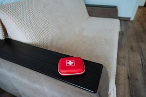 A bright red first aid kit is currently resting comfortably on the arm of a cozy couch, ensuring easy access to quick aid whenever needed in a stylish living space designed for comfort photo