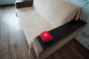 A vibrant red box, prominently marked with a distinctive cross symbol, is positioned atop a cozy couch located within a stylish living room environment, creating an inviting atmosphere photo