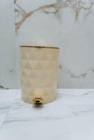 A chic trash can with a shiny gold handle is placed on a polished marble countertop, blending aesthetics and functionality to enhance the decor and ambiance of the space photo