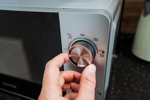 A person is slowly turning a knob on the microwave oven, which is an essential kitchen appliance specifically designed for quickly cooking and reheating various types of food with ease photo