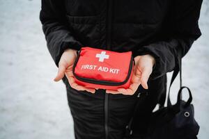 A person stands confidently, holding a vibrant red first aid kit that indicates preparedness, ready to assist in emergencies and ensure the utmost safety for anyone in urgent need photo