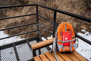 A bright orange backpack is currently resting on a sturdy wooden bench that is strategically positioned next to a railing, creating a picturesque and charming scene on a chilly winter day photo