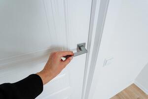A person is skillfully opening a white door that features a shiny and elegant silver handle, which clearly indicates that they are gaining access to another area or section of the house photo