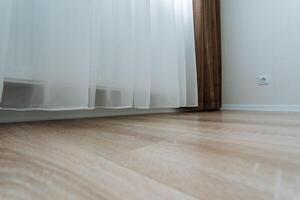 The room features a beautiful wooden floor, complemented by a white curtain gracefully hanging at the window, creating a warm and inviting atmosphere for anyone who enters photo