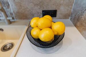 A bowl filled with fresh, vibrant lemons is placed on a counter that is conveniently positioned next to a kitchen sink, adding a bright, refreshing touch to the kitchen decor photo