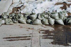 A sizable pile of sandbags is currently positioned on the side of a road, presumably for purposes related to construction or safety measures during adverse weather conditions photo