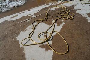 A bright yellow hose is currently laying flat on a damp concrete surface, glistening slightly from the moisture that has settled on it after perhaps a recent rain shower photo