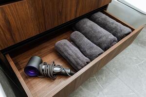 A meticulously organized bathroom cabinet features a drawer that is filled with neatly arranged towels and a conveniently placed hair dryer, perfect for all your grooming and styling needs photo