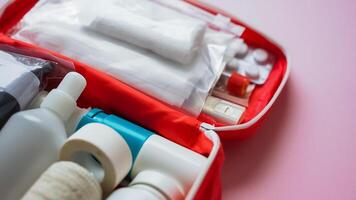 A vibrant red first aid kit is generously filled with various bottles and pills, all resting on a soft pink surface, showcasing a rich and inviting contrast of colors and textures photo