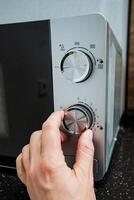 A person is turning a knob on a microwave, which is a widely used kitchen appliance known for its ability to efficiently heat and cook food while maintaining both flavor and texture photo
