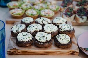 A beautifully crafted wooden cutting board is adorned with delectable stuffed mushrooms, generously covered in a rich layer of melted cheese, making for a delightful appetizer photo