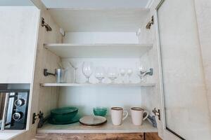 Inside a kitchen cabinet, you will find a variety of dishes, including plates, cups, and glasses neatly organized on the shelves. Its a space designed for both functionality and style photo