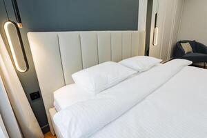 Inside a hotel room, there is a cozy bed adorned with crisp white sheets and plush pillows arranged neatly, creating an inviting atmosphere for guests to relax and unwind photo