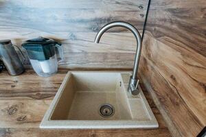 In the kitchen area, there is a sink equipped with a faucet, accompanied by a pitcher, all elegantly arranged on a wooden countertop that enhances the overall aesthetic of the space photo