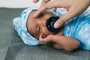 Anonymous mother with newborn baby wrapped on soft blanket with pacifier photo