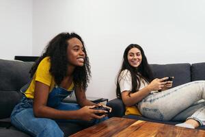 Two young women sitting on a couch playing games and having fun photo