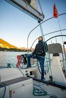 Young man captain standing at helm and controls sailboat during a journey by sea in winter time in Montenegro photo