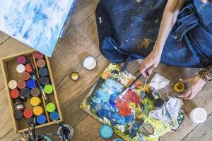 A woman is painting on a wooden floor with paint and brushes photo