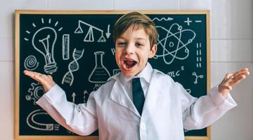 A young boy in a lab coat standing in front of a chalkboard photo