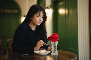 Asian Young woman enjoying dessert with coffee in a cozy cafe setting with green walls and flowers on the table photo