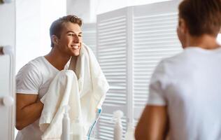 Everyday Routine Concept. Good-looking man wiping his face with towel while standing in modern bathroom photo