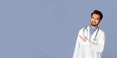 Smiling Indian doctor in uniform showing something over violet background photo