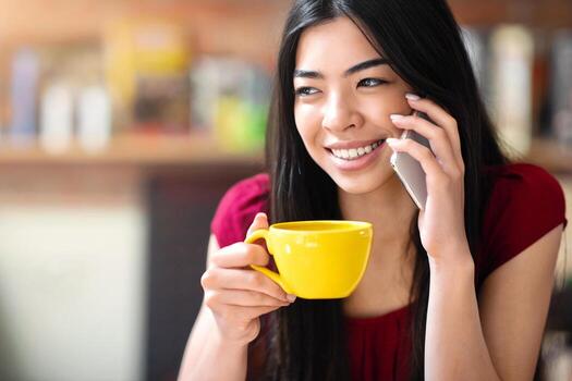 Cheerful Corean Girl Relaxing In Cafe, Talking On Cellphone And Drinking Coffee, Having Pleasant Concersation, Enjoying Mobile Communication, Closeup Image With Selective Focus And Free Space photo