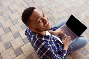 Above view of black man using personal computer sitting on the stairs in city, looking at camera, mock up photo