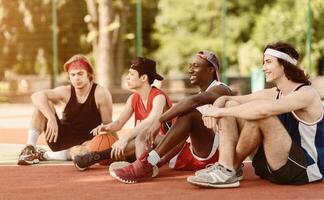 Diverse team of professional basketball players talking during their break from game at outdoor arena, copy space photo