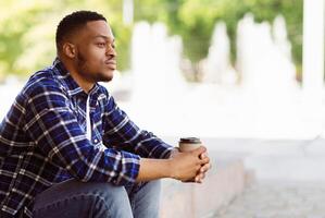 Side view of pensive african american person sitting in the park with coffee, looking aside, free space photo