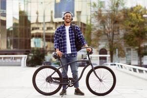 Full length portrait of african american guy wearing headset, standing with his bicycle, selective focus photo