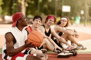 Young African American basketballer and his diverse team relaxing before match at outdoor court, free space. Group of multiethnic players having fun, chatting to each other after game photo