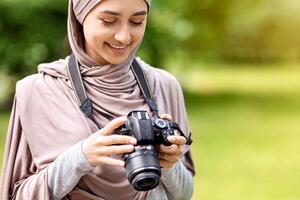 Arab woman photographer working at public park, checking on taken photos, copy space photo