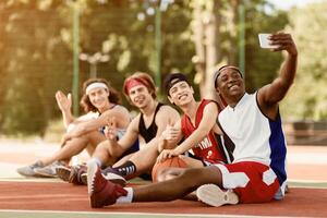 Group of happy basketball players taking selfie while resting after game at outdoor arena, copy space photo