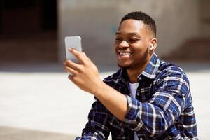 Portrait of handsome black guy making call on cell phone, watching something or taking selfie in the park photo