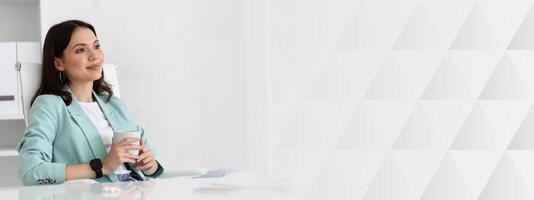 Calm dreaming smiling millennial caucasian lady in suit resting at workplace with cup of tea and computer, look at free space in office interior. Coffee break, business with device, work, relax photo