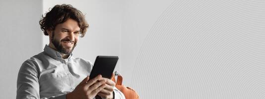 Happy mature businessman using tablet pc, looking at screen, sitting on bean bag chair in modern office, empty space. Confident entrepreneur checking email, reading news, browsing internet photo