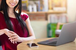 Confident Young Asian Woman Sitting At Table In Cafe With Laptop And Smartphone, Portrait Of Smiling Female Freelancer Posing In Cafeteria While Working Remotely On Computer, Copy Space photo