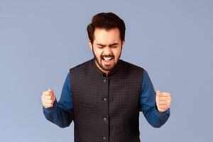Furious Indian man clenching fists in anger and screaming on lilac background, panorama photo