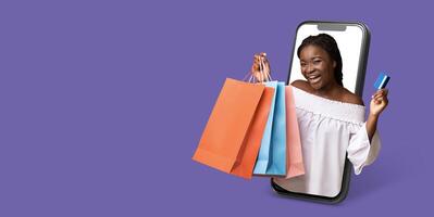 A joyful buyer engages in online shopping using a smartphone with a large screen. She holds colorful shopping bags and a credit card, showcasing the convenience of e-commerce. photo