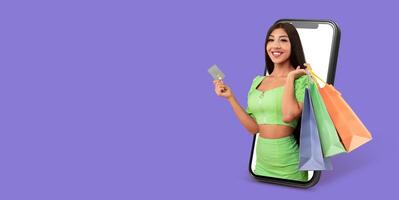 A buyer engages in online shopping using a smartphone. She holds a credit card and shopping bags, showcasing the convenience of mobile commerce against a solid color background. photo