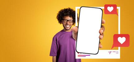 An enthusiastic influencer stands against a vibrant yellow background, proudly holding a smartphone displaying a blank screen, ready for social media interaction and chatting about trends. photo