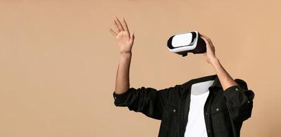 A person enjoys a virtual reality experience, wearing a headset and waving their hand. The background is a solid beige, emphasizing the focus on the user and their interaction with virtual worlds. photo