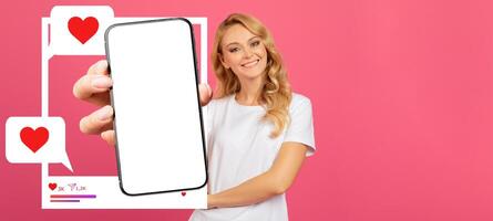A social media influencer smiles while holding a smartphone in front of a bright pink background. The device displays a blank screen, inviting viewers to imagine their own content. photo