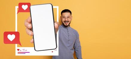 A smiling influencer holds a smartphone in front of a plain yellow background, showcasing a blank screen ready for social media interactions, expressing excitement and engagement online. photo